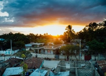 A picturesque rural village captured at sunset with a vibrant sky and silhouetted trees.