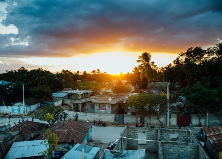A picturesque rural village captured at sunset with a vibrant sky and silhouetted trees.
