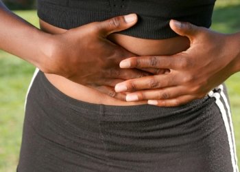 A woman holding her stomach outdoors indicating possible abdominal discomfort or pain.