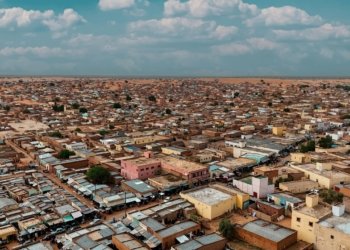 Aerial panorama of a sprawling desert townscape with flat-roofed buildings under a bright sky.