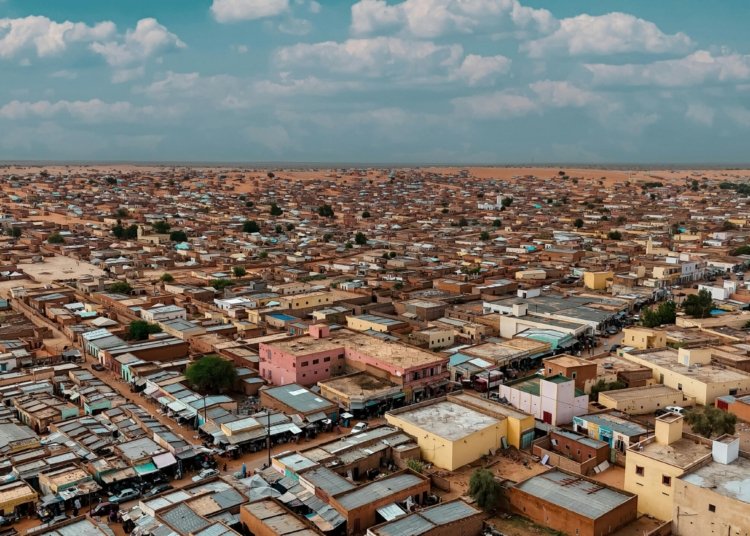 Aerial panorama of a sprawling desert townscape with flat-roofed buildings under a bright sky.