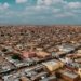 Aerial panorama of a sprawling desert townscape with flat-roofed buildings under a bright sky.