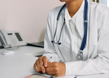 Doctor with stethoscope and white coat seated at a clinic desk.