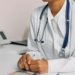 Doctor with stethoscope and white coat seated at a clinic desk.