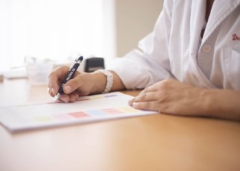 Close-up of a female doctor writing a prescription at a desk in an office setting.