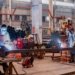 Two welders wearing protective gear working in a busy industrial factory workshop.