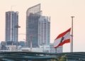 Urban skyline of Beirut with a prominent Lebanese flag gently waving at sunset.