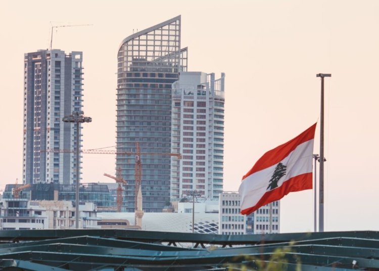 Urban skyline of Beirut with a prominent Lebanese flag gently waving at sunset.