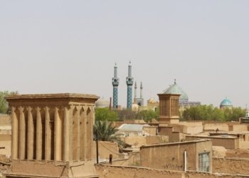 View of Yazd's historic architecture with windcatchers and blue mosque domes under a clear sky.