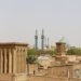 View of Yazd's historic architecture with windcatchers and blue mosque domes under a clear sky.