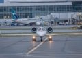 A private jet on the runway at a bustling airport with commercial planes and terminal in view.