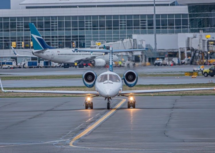 A private jet on the runway at a bustling airport with commercial planes and terminal in view.
