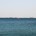 A tranquil ocean view featuring several cargo ships on the horizon under a clear sky.