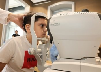Young boy receiving an eye exam using autorefractor at a clinic. Healthcare concept.