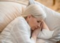 A mature woman in a reflective mood rests peacefully on a pillow indoors.