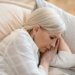 A mature woman in a reflective mood rests peacefully on a pillow indoors.