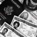 A black and white composition of a US passport, visas, and currency, showcasing travel essentials.