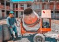 A construction worker operating a concrete mixer at an active building site, emphasizing safety gear.