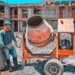 A construction worker operating a concrete mixer at an active building site, emphasizing safety gear.