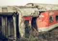 A dilapidated train carriage lying abandoned in an overgrown field after derailing.