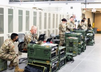 A group of military personnel in uniforms using computers and communication equipment in a secure indoor facility.