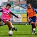 Action shot of women playing soccer in colorful uniforms on a sunny day.
