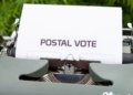 Close-up of typewriter with paper displaying the words 'Postal Vote', outdoors.