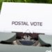 Close-up of typewriter with paper displaying the words 'Postal Vote', outdoors.