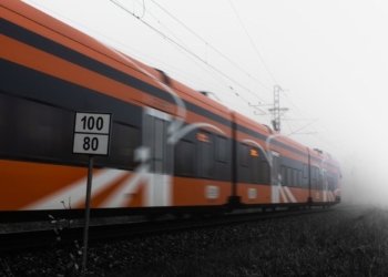 Orange train speeding on railway tracks in dense fog with speed sign visible.