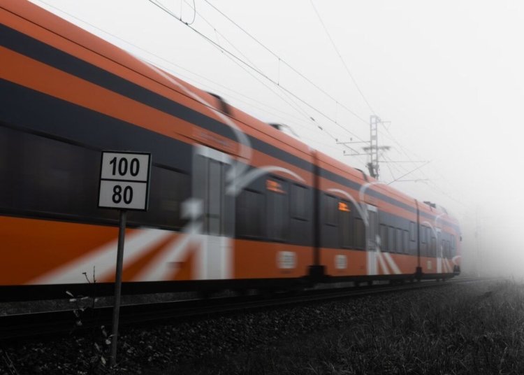 Orange train speeding on railway tracks in dense fog with speed sign visible.