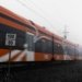 Orange train speeding on railway tracks in dense fog with speed sign visible.