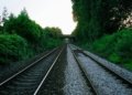 Railway tracks in rural UK surrounded by greenery under a bridge at sunset.
