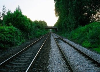 Railway tracks in rural UK surrounded by greenery under a bridge at sunset.