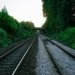 Railway tracks in rural UK surrounded by greenery under a bridge at sunset.