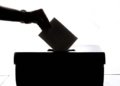 Silhouette of a hand placing a vote into a ballot box, symbolizing democracy.