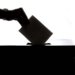 Silhouette of a hand placing a vote into a ballot box, symbolizing democracy.
