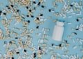 Top view of various pills scattered around a white bottle on a blue surface.