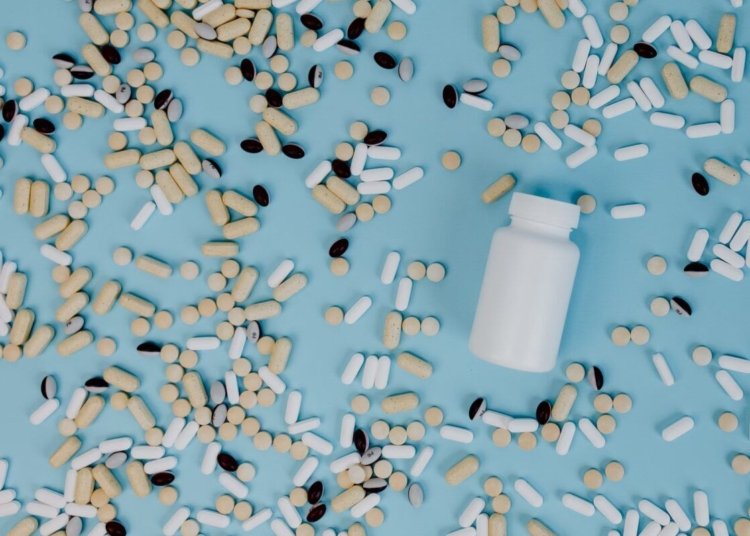 Top view of various pills scattered around a white bottle on a blue surface.