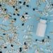 Top view of various pills scattered around a white bottle on a blue surface.
